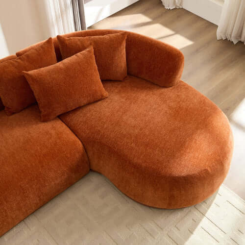 Top view of rounded L-shaped chaise sofa in rich orange color with plush pillows, perfect for a cozy living space.