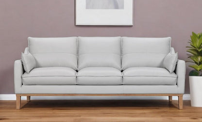 87" Gray Leather Sofa And Toss Pillows With Brown Legs in a stylish living room setting.
