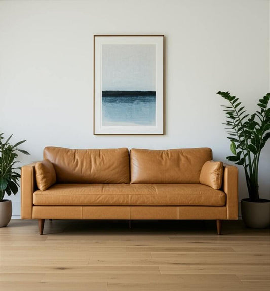 88" Tan Leather Sofa And Toss Pillows With Brown Legs against a minimalist backdrop with plants and artwork.