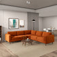A modern living room featuring the Ashcroft Furniture Amber MCM Corner Sectional Sofa 103 in orange on a beige rug, paired with a round wooden coffee table, wall art, wood floors, neutral walls, and an open dining area in the background.