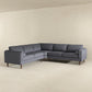 The Amber MCM Corner Sectional Sofa 103 by Ashcroft Furniture, featuring wooden legs, is placed in the corner of a minimalist room with light beige walls and flooring to highlight its premium craftsmanship.