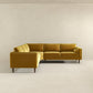 The Amber MCM Corner Sectional Sofa 103 by Ashcroft Furniture, shown here in mustard yellow with wooden legs, brings modern style and premium craftsmanship to a minimalist room with light beige walls and floor.