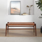 The Cody MCM Strapped Genuine Leather Bench 44 by Ashcroft Furniture sits on a light wood floor in a minimalist room, with a shelf holding décor and a leafy plant in the corner.