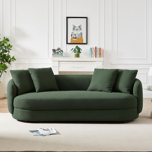 A modern living room with Parisian elegance, featuring the Ashcroft Dylan Modern Bohemian French Boucle Sofa in dark green, four matching cushions, a white rug, potted plant, books, and a framed cat print above a white mantel.