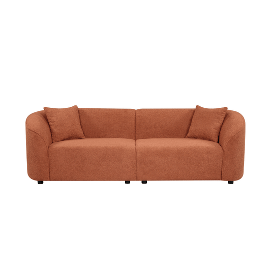 Contemporary sloped arm boucle upholstered sofa in rust color, featuring a sculptural curved design and plush cushions.