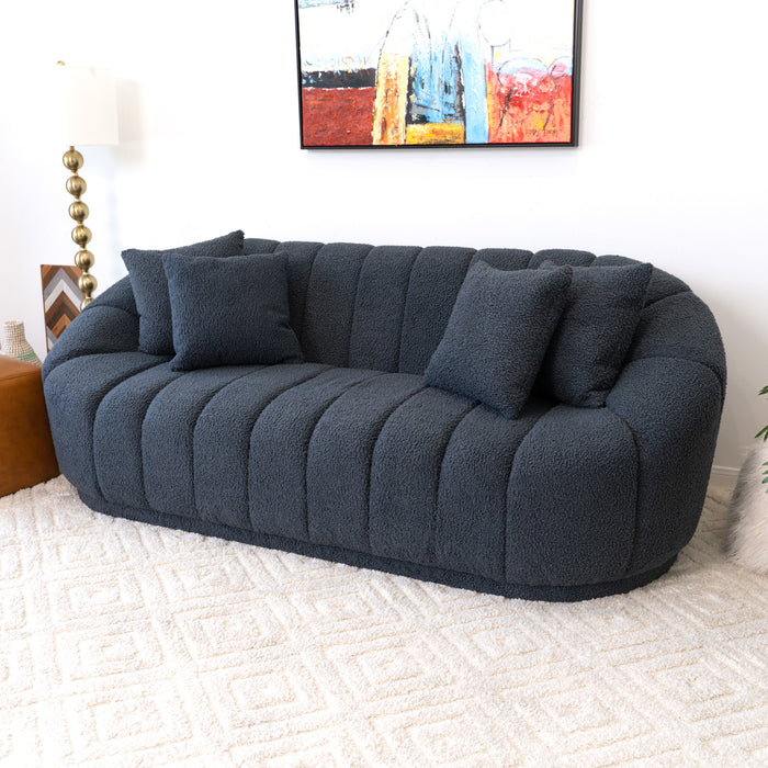 The Maximilian Japandi Channel Tufted Boucle Sofa 86” by Ashcroft Furniture in modern dark gray features three matching pillows and sits on a light patterned rug, complemented by a colorful abstract painting and a gold-based lamp for sustainable luxury ambience.