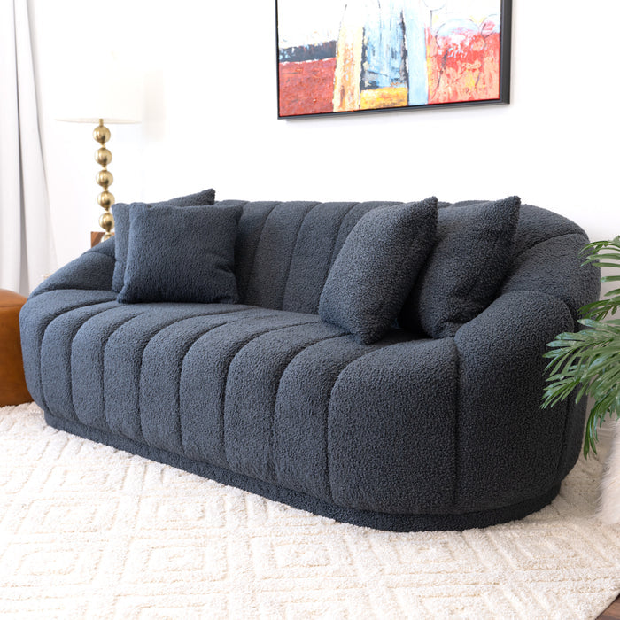 The Ashcroft Furniture Maximilian Japandi Channel Tufted Boucle Sofa 86”, in dark gray with two matching pillows, sits on a cream rug. A leafy plant, floor lamp, and colorful painting complete this elegant, sustainable space.
