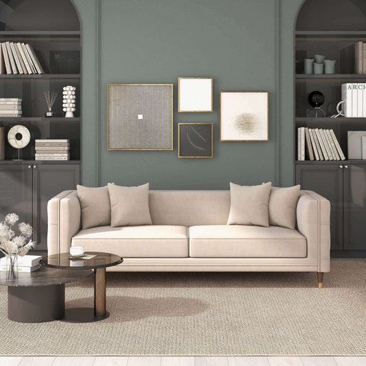 A modern living room features the Ashcroft Furniture Edward MCM Elegant Tufted Velvet Sofa 90 in beige, light cushions, a round coffee table, dark built-in shelves with books and decor, and framed minimalist art on a green wall. The space looks tidy and stylish.