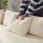 Person arranging a plush white pillow on a creamy sofa with soft fabric, showcasing comfort and style.