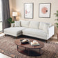 A modern living room features the Ashcroft Furniture Blake Velvet Upholstered L-Shape Chaise Sofa Sectional 107 in white, paired with a dark wood oval coffee table, abstract wall art, a floor lamp, decorative books, and plants on a patterned rug.