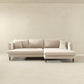 The Blake Velvet Upholstered L-Shape Chaise Sofa Sectional 107 by Ashcroft Furniture, with plush velvet, reversible chaise, four back cushions, and two accent pillows, is set in a minimalist room with beige walls and floor.
