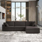 A modern living room features the Ashcroft Furniture Cecilia Dark Gray Modular Chaise Sofa Sectional 121 with a reversible chaise and two pillows, set amid large windows, a statement chandelier, bookshelves, a desk, and a neutral patterned rug.