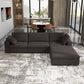 A modern living room with the Ashcroft Furniture Cecilia Dark Gray Modular Chaise Sofa Sectional 121 on a patterned rug, floor-to-ceiling windows, a dining table with tan chairs, and city buildings visible outside.