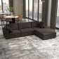 A modern living room showcases the Ashcroft Furniture Cecilia Dark Gray Modular Chaise Sofa Sectional 121 on a patterned rug by floor-to-ceiling windows with city views, while a dining table with chairs is arranged in the background.