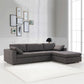 A bright living room with large windows features the Ashcroft Furniture Cecilia Dark Gray Modular Chaise Sofa Sectional 121, a reversible chaise, white shag rug, black table lamp on a side table, and a gallery wall of framed art against white walls.