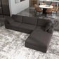 A modern living room features the Ashcroft Furniture Cecilia Dark Gray Modular Chaise Sofa Sectional 121 with a reversible chaise on a patterned rug, adjacent to a dining area with a round white table and tan chairs atop glossy marble flooring.