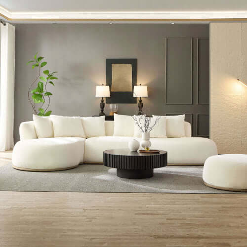 Cozy white rounded L-shaped chaise sofa sectional in a modern living room with a black coffee table and greenery.