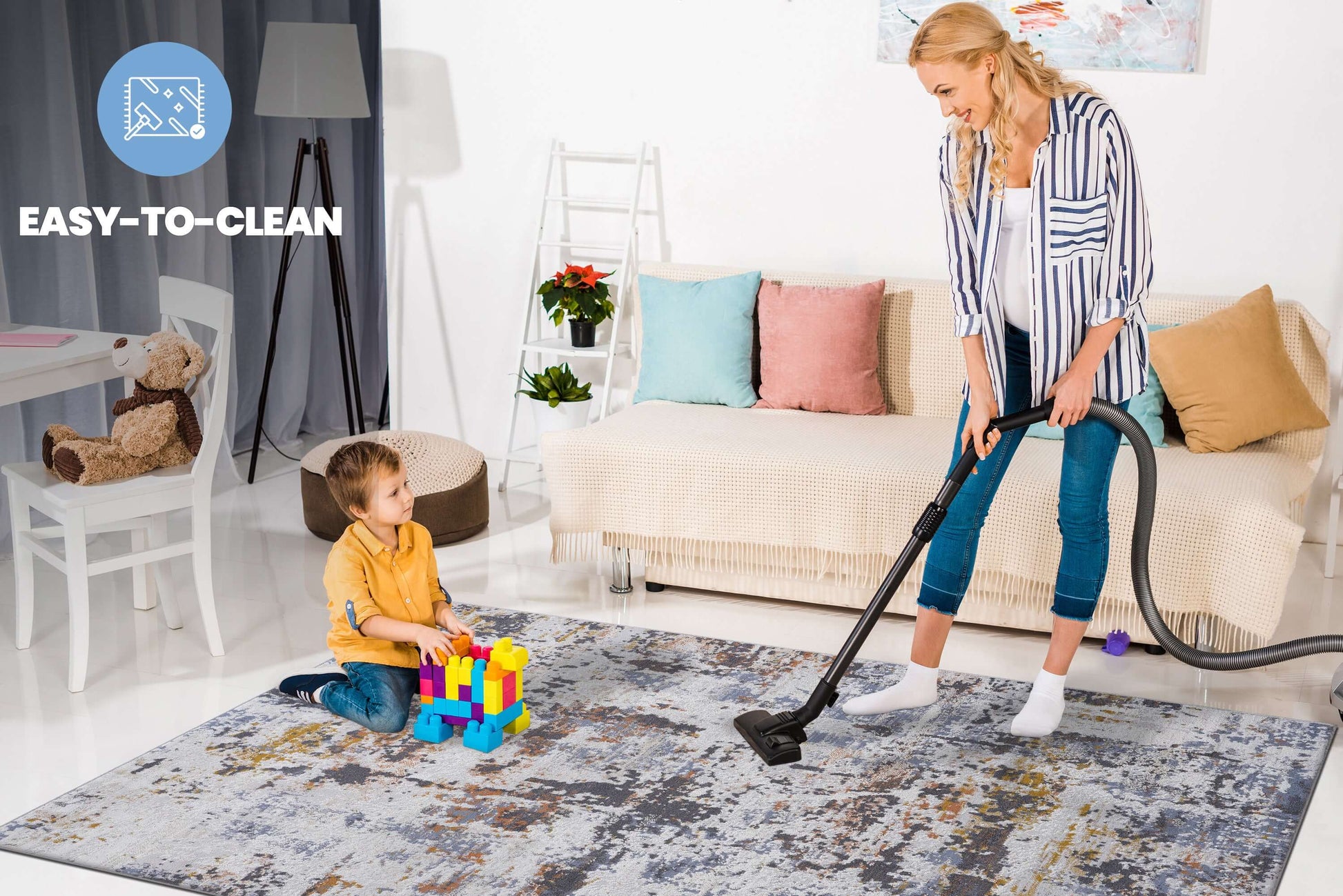 Woman vacuuming multicolor abstract area rug while child plays with blocks, showcasing easy cleaning feature.