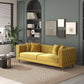 Modern living room with Ashcroft Furnitures Edward MCM Elegant Tufted Velvet Sofa 90 in mustard yellow, four matching cushions, textured rug, round coffee tables, wall art, and built-in shelves against a muted green-gray wall.
