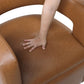 MCM Faux Leather Swivel Chair – Modern Barrel Accent Chair (2 Colors) featuring a hand pressing on the camel-tone faux leather seat.