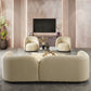 A modern living room featuring the Ashcroft Furniture Donna Minimalist Curved Boucle Sofa 93 in cream, with armchairs, a round glass coffee table, marble walls, minimalist decor, potted plants, and a TV on a built-in cabinet.