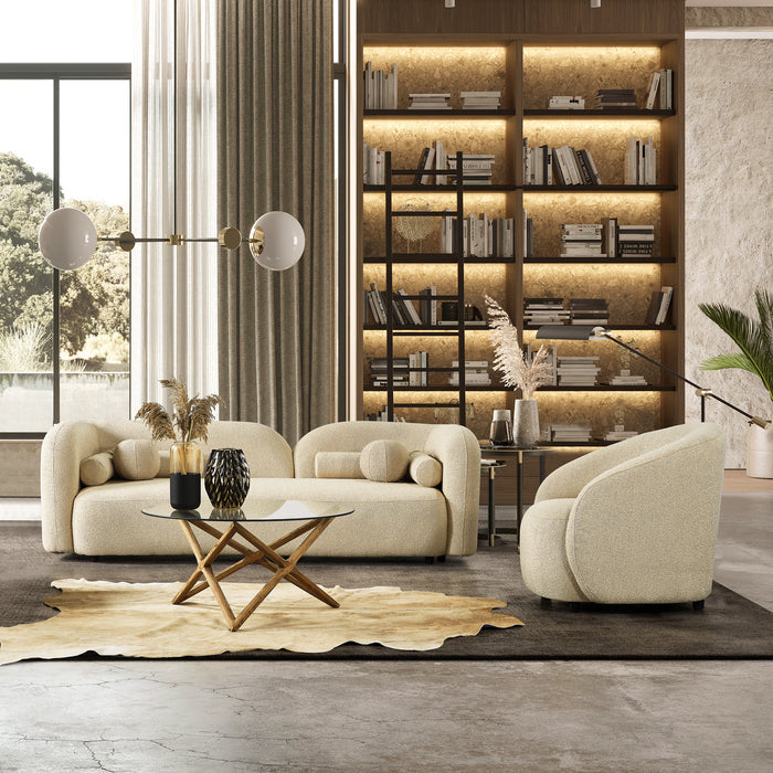 A modern living room featuring the Donna Minimalist Curved Boucle Sofa 93 by Ashcroft Furniture, a glass coffee table with a wooden base, cowhide rug, large draped windows, and built-in bookshelves with warm lighting and decor.