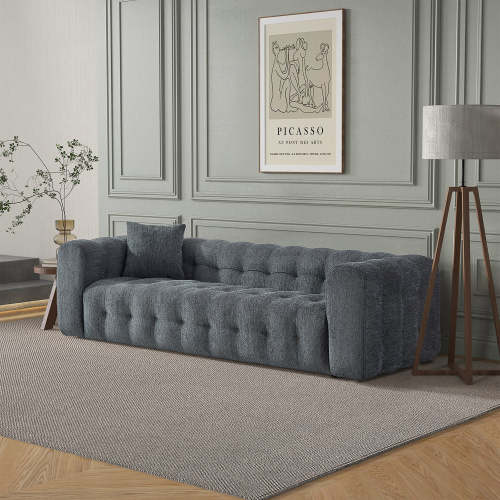 A modern living room featuring the Ashcroft Furniture Eden Modern Boucle Bubble Sofa 90, a floor lamp with a gray shade, a framed Picasso print, and a small plant on a side table. Decorative paneling on the light gray walls adds glamour.