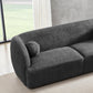 The Anna Boucle Fabric Upholstered Sofa 87 by Ashcroft Furniture, shown in dark gray with textured boucle fabric and a matching round cushion, sits in a bright room with light wood floors, a beige rug, and floor-to-ceiling windows.