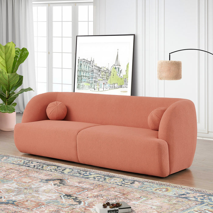 A modern living room features the Anna Boucle Fabric Upholstered Sofa (87, Peach) by Ashcroft Furniture, two round cushions, a patterned rug, floor lamp, green potted plant, and framed artwork near large windows and a white wall.