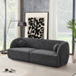 A modern living room featuring the Ashcroft Furniture Anna Boucle Fabric Upholstered Sofa 87 in dark gray, two round pillows, a black standing lamp, abstract black-and-white art, a large plant, and floor-to-ceiling windows with white curtains.