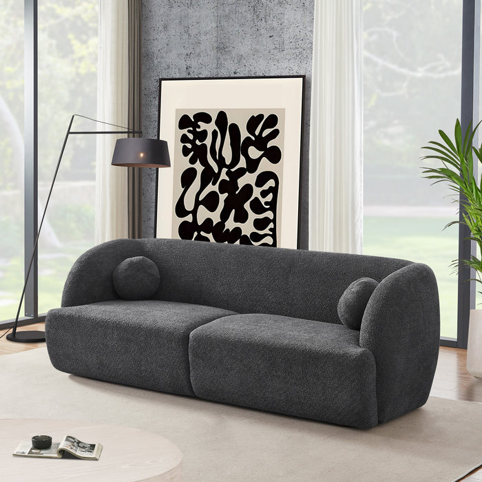 A modern living room featuring the Ashcroft Furniture Anna Boucle Fabric Upholstered Sofa 87 in dark gray, two round pillows, a black standing lamp, abstract black-and-white art, a large plant, and floor-to-ceiling windows with white curtains.