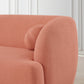 Close-up of the Anna Boucle Fabric Upholstered Sofa 87 in coral from Ashcroft Furniture, featuring a modern curved design with a matching round pillow—an elegant addition to any light-paneled room with wooden floors.