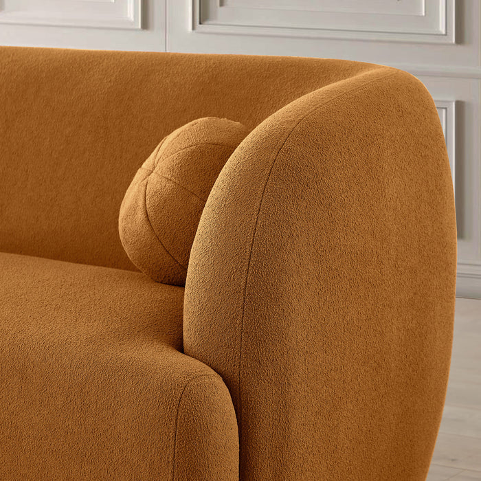 Close-up of the Anna Boucle Fabric Upholstered Sofa 87 by Ashcroft Furniture in orange-brown with a matching round cushion, set against a light paneled wall, highlighting its modern elegance.