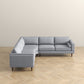 The Amber MCM Corner Sectional Sofa 103 by Ashcroft Furniture, shown in light gray, features premium craftsmanship and wooden legs, set on a light wood herringbone floor against a plain beige wall.