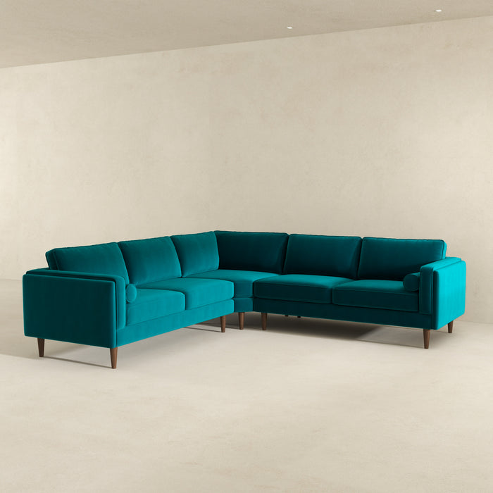 The Amber MCM Corner Sectional Sofa 103 by Ashcroft Furniture features clean lines and wooden legs, highlighting premium craftsmanship in a minimalist, light-toned room with plain walls and flooring. Available in 5 colors.