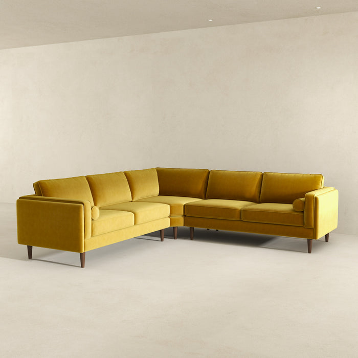 The Amber MCM Corner Sectional Sofa 103 by Ashcroft Furniture, shown here in yellow with wooden legs and bolster pillows, highlights premium craftsmanship in a spacious, minimalist room with light walls and floors.