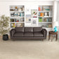 A modern living room featuring the Ashcroft Furniture Chase MCM Genuine Leather Sofa 91, a beige woven rug, round wooden side table with turquoise lamp, potted plant, and white bookshelves filled with books and décor for mid-century flair.