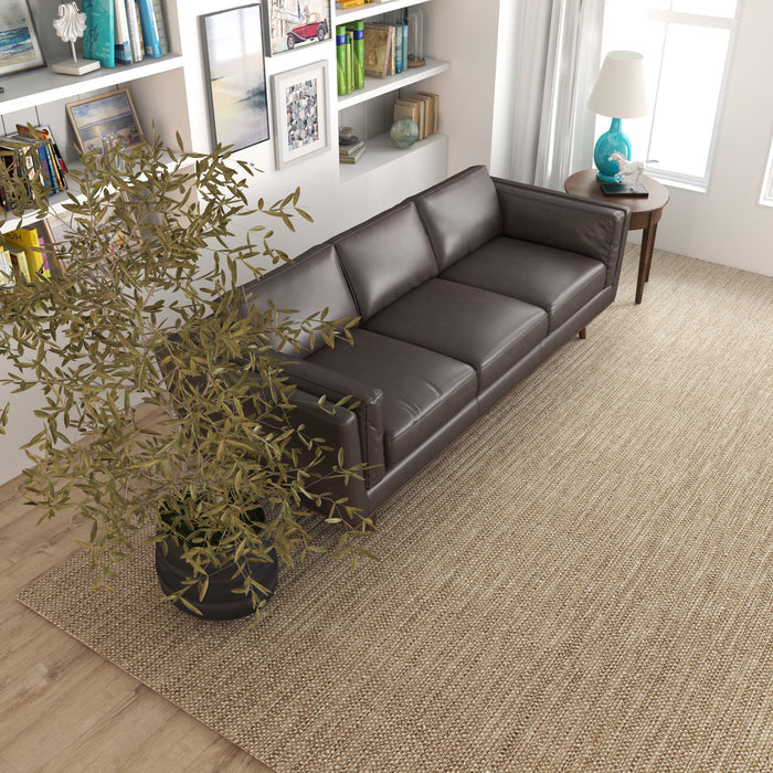 A modern living room features the Ashcroft Furniture Chase MCM Genuine Leather Sofa 91 in dark brown, a large potted plant, beige woven rug, bookshelves with decor, and a window with white curtains letting in natural light.