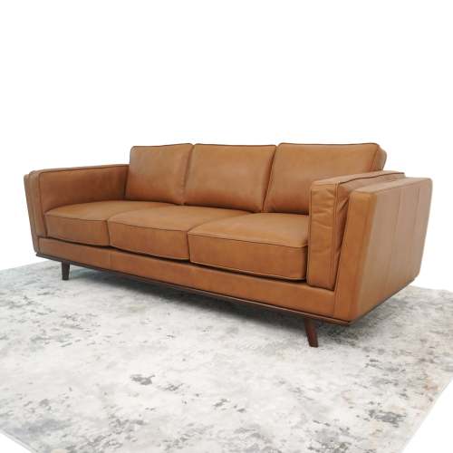 The Ashcroft Furniture Chase MCM Genuine Leather Sofa 91, featuring three seat cushions and angled armrests, sits on a light-colored, slightly distressed area rug.