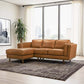 A modern living room with the Ashcroft Furniture Chase MCM Tan Leather Chaise Sofa Sectional 92, a geometric rug, sheer-curtained large windows, a tall green plant, and framed black-and-white photo art on the wall.