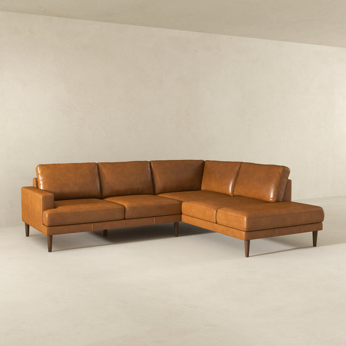 The Ashcroft Furniture Corbin MCM Tan Leather Sectional Chaise Sofa 108 features a mid-century modern L-shape and wooden legs, shown in a minimal, empty room with light walls and flooring.