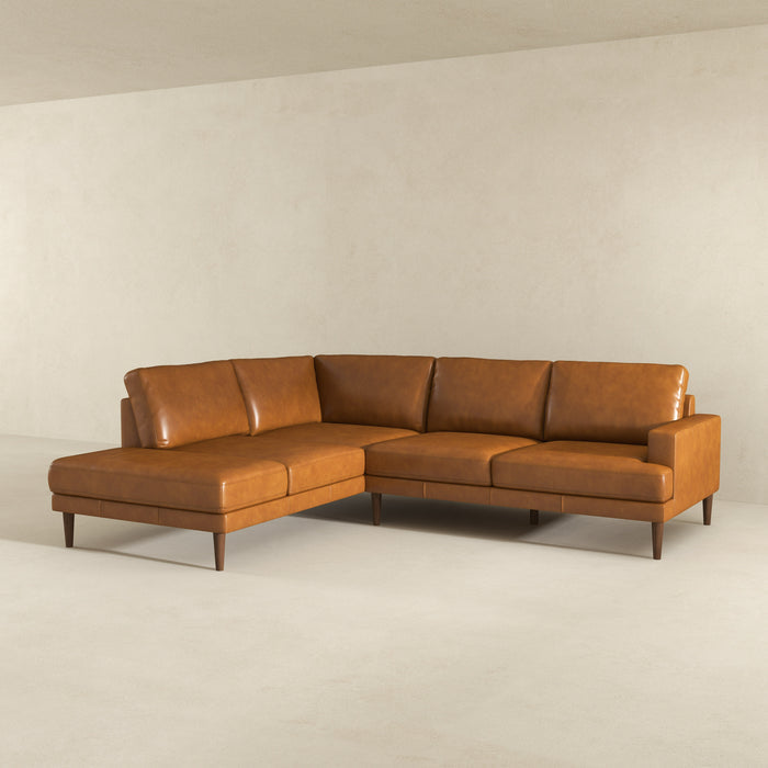 The Corbin MCM Tan Leather Sectional Chaise Sofa by Ashcroft Furniture features caramel leather upholstery and wooden legs, adding modern style to a minimal, light beige room with bare walls and floor.
