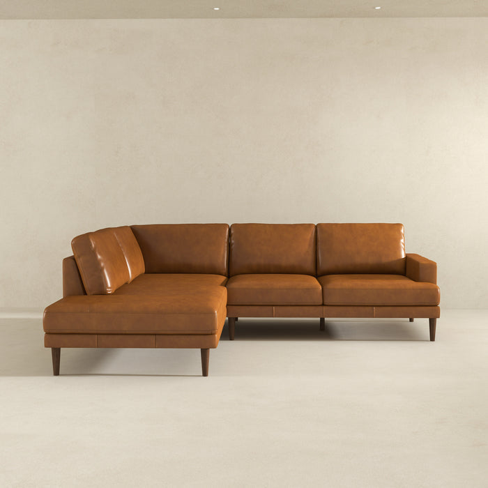 The Corbin MCM Tan Leather Sectional Chaise Sofa 108 by Ashcroft Furniture features clean lines and wooden legs, adding mid-century modern style against a light wall in this minimalist room.