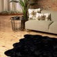 Scalloped black faux fur shag rug on wooden floor in modern living room with plants and stylish decor.