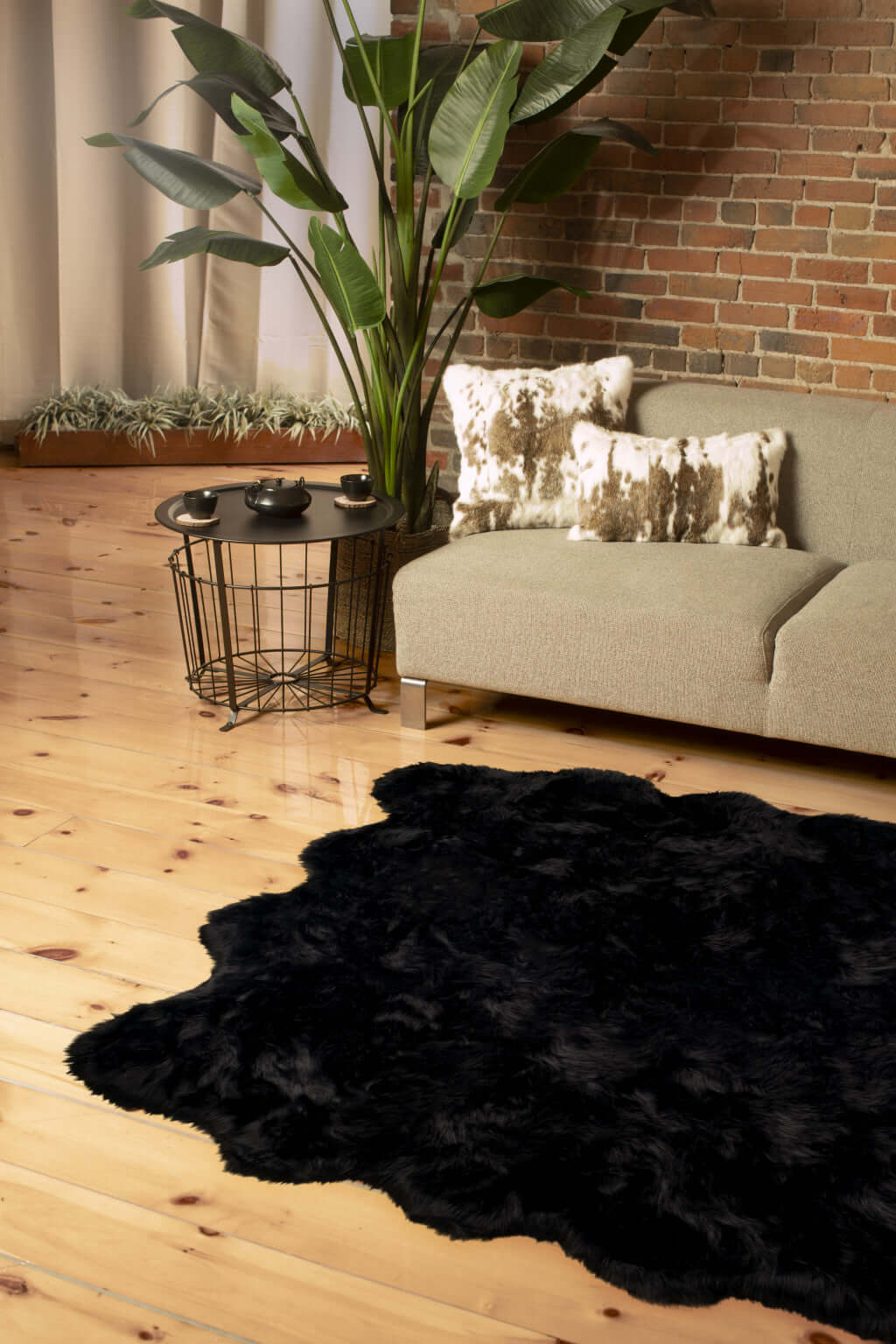 Scalloped black faux fur shag rug on wooden floor in modern living room with plants and stylish decor.
