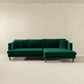 The Blake Velvet Upholstered L-Shape Chaise Sofa Sectional 107 by Ashcroft Furniture, with plush velvet upholstery, wooden legs, and matching cushions, adds elegance to a minimalist room with beige walls and a light floor.