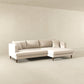 The Ashcroft Furniture Blake Velvet Upholstered L-Shape Chaise Sofa Sectional 107 in light beige, featuring plush velvet, wooden legs, three back cushions, two throw pillows, and a reversible chaise, adds modern style to a minimalist room with off-white walls and floor.
