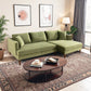 A living room with the Ashcroft Furniture Blake Velvet Upholstered L-Shape Chaise Sofa Sectional 107, four cushions, a round wooden coffee table with books and decor, two framed wall art pieces, a patterned rug, plants, a floor lamp, and window curtains.