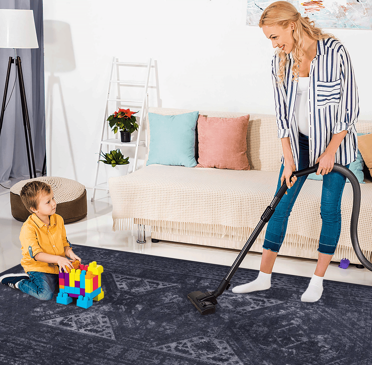 Mom vacuuming black washable rug while child plays with building blocks in a stylish living room.