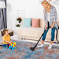 A woman vacuuming a colorful abstract area rug while a child plays with building blocks nearby.